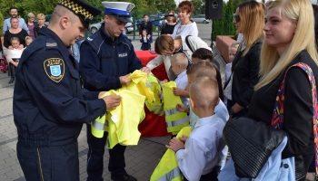 policjanci i straznik miejski wręczają kamizelki odblaskowe pierwszoklasistom